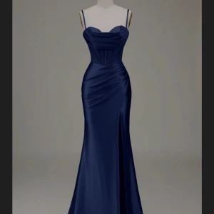 Marinblå långklänning med snörning och slits - Säljer en elegant marinblå långklänning i satin med smala axelband, draperad byst och figurnära passform. Klänningen har snörning i ryggen och en hög slits framtill som ger en snygg siluett. Perfekt för bal eller fest!