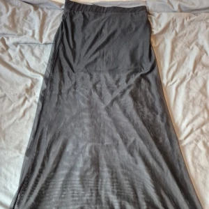 Svart långkjol från Divided - Säljer en svart långkjol från Divided. Kjolen har en lätt transparent nederdel och resår i midjan för en bekväm passform. Perfekt för dig som gillar en enkel men snygg stil. Materialet är polyester.