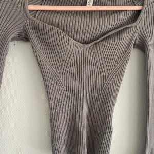 Grå ribbad topp från H&M - Säljer en grå ribbad topp från H&M med lång ärm och snygg v-ringning. Toppen har en figurnära passform och markerade sömmar framtill som ger en cool look.