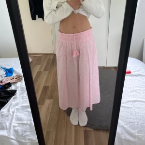 Ljusrosa långkjol  - Supersöt ljusrosa långkjol från Gina Tricot med dekorativa tofsar. Kjolen har ett rosa vittmönster och är gjord i ett lätt och luftigt material, perfekt för varmare dagar. Säljer för att den är för kort, priset går att diskuteras!
