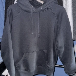 Svart hoodie från BikBok - En klassisk svart hoodie från BikBok med huva och dragsko. Tröjan har en stor magficka framtill och ribbade muddar vid ärmslut och nederkant. Perfekt för en avslappnad stil.