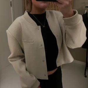 Beige croppad cardigan jacka - Snygg beige croppad cardigan jacka med rund halsringning och tryckknappar framtill. Jackan har långa ärmar och en minimalistisk design som passar perfekt till många outfits. Jackan är aldrig använd!😊