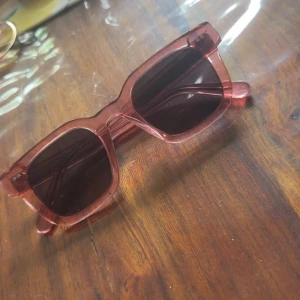 Rosa fyrkantiga solglasögon - Snygga solglasögon med transparent rosa båge och mörka glas. Modellen har en trendig, fyrkantig form som ger en cool retrovibe. Perfekt accessoar för att lyfta din stil under soliga dagar.
