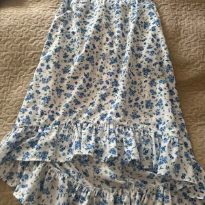 Blommig kjol med volang från Pieces - Söt vit kjol med blått blommönster från Pieces. Kjolen har volangdetalj nertill och är perfekt för sommarens alla tillfällen. Lätt och luftig modell med normal passform. Skriv för mer info/ fler bilder🫶🏻 storlek M💞 helt oanvänd🩷