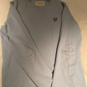 Ljusblå tröja från Lyle & Scott - Säljer en ljusblå långärmad tröja från Lyle & Scott i storlek S. Tröjan har rund halsringning och den klassiska gula loggan broderad på bröstet. Tillverkad i ett mjukt material som passar perfekt till vardags.