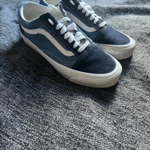 Blå och vita sneakers från Vans - Säljer ett par klassiska Vans sneakers i blått och vitt med vit sula och snörning. Skorna har den ikoniska sidoremsan och rund tå. Perfekta för en avslappnad och stilren look.