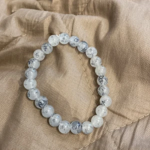 Elastiskt armband med vita och gråmelerade pärlor - Säljer ett snyggt armband med runda pärlor i vitt och grått, med marmorerad effekt. Armbandet är elastiskt och passar de flesta handleder. Perfekt accessoar för att lyfta din stil!