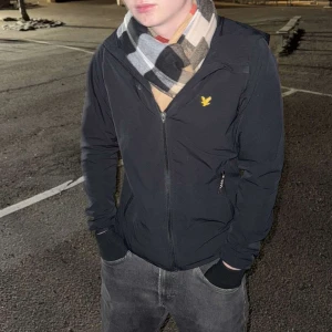 Rutig halsduk från Burberry - Säljer en klassisk rutig halsduk från Burberry i beige, svart, vit och röd. Tillverkad i 100% kashmir för en lyxig och mjuk känsla. Perfekt accessoar för att hålla dig varm och stilren under kyliga dagar.