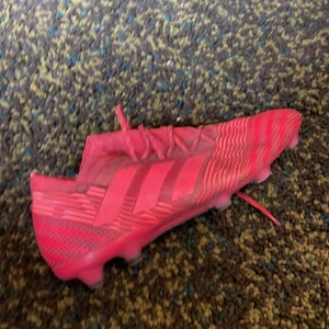 Röda fotbollsskor från Adidas - Säljer ett par röda fotbollsskor från Adidas med klassiska ränder på sidan. Skorna har snörning och mönstrad ovandel för extra grepp. Inte så mycket slitage och använda i ungefär en säsong.