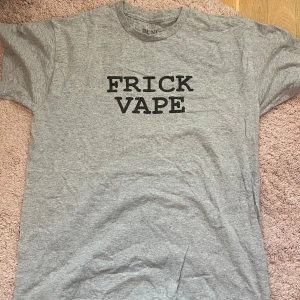 T-shirt Baylen Levine - Grå t-shirt från Benitez by Baylen Levine med svart texttryck 'FRICK VAPE' på bröstet. Klassisk rund halsringning och normal passform. Perfekt för dig som gillar statement-plagg och enkel stil. 