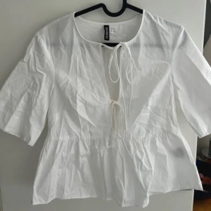Vit blus med knyt - Säljer en vit blus från hm med knyt framtill och v-ringning. Blusen har korta ärmar och en lätt volang nedtill. Perfekt för vår och sommar!
