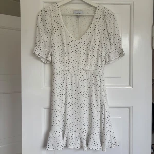 Vit prickig klänning från & Other Stories - Söt vit kortklänning från & Other Stories med  svarta prickar, v-ringning och volangkant nertill.  Perfekt till sommaren.