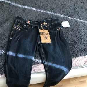 Mörkblå jeansbyxor med kontrastsömmar från DS Style - Säljer ett par mörkblå jeansbyxor från D6 soul.  med snygga  detaljerade fickor både fram och bak. Klassisk femficksmodell med knapp och dragkedja. Perfekta för dig som gillar en stilren men ändå unik look. Dom är lågmidjade och helt oanvända. Säljer då dom inte passar mig som bär storlek S. Jag köpte dom för 699