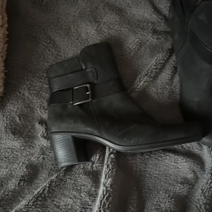 Svarta boots med spänne från Ecco - Säljer ett par svarta boots från Ecco med snyggt spänne på sidan och låg klack. Skorna har rund tå och dragkedja på insidan för enkel påtagning. Perfekta till höst och vinter! Nästan aldrig använda.