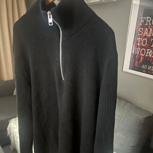 Svart stickad tröja med dragkedja från Jack & Jones - Säljer en svart stickad tröja från Jack & Jones med hög krage och dragkedja framtill. Tröjan har ribbad struktur och lång ärm, perfekt för kyligare dagar. Enkel och stilren design som passar till det mesta.