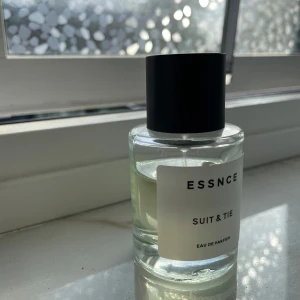 ESSNCE Suit & Tie Eau de Parfum - Fräsch parfym från ESSNCE med namnet Suit & Tie. Flaskan är genomskinlig med svart lock och enkel vit etikett. Doften är elegant och passar perfekt för dig som gillar stilrena och moderna parfymer.