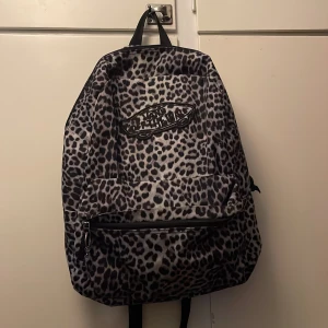 Leopardmönstrad vansryggsäck - Säljer en ryggsäck från Vans med grått och svart leopardmönster. Väskan har ett stort huvudfack, en mindre ficka framtill med dragkedja och justerbara axelband.