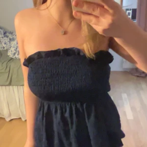 Marinblå axelbandslös klänning - Säljer en marinblå axelbandslös topp med smockad överdel och volangdetalj upptill. 