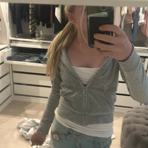 Grå hoodie från Juicy Couture - Säljer en ljusgrå hoodie från Juicy Couture i mjuk bomullsblandning. Tröjan har dragkedja framtill, huva och två fickor. Klassisk och enkel design med liten logga på bröstet. Perfekt för en avslappnad stil.