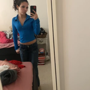 Blå croppad långärmad tröja med dragkedja - Säljer en blå croppad långärmad tröja med krage och dragkedja framtill. Tröjan har en tight passform och är perfekt för dig som gillar en sportig och trendig stil.