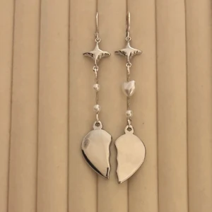 Silverfärgade örhängen med hjärtmotiv - Unika silverfärgade örhängen med stjärndetalj upptill, små pärlor och ett delat hjärta längst ner. Perfekta för dig som vill sticka ut med ett coolt och romantiskt smycke. Aldrig använda!❤️