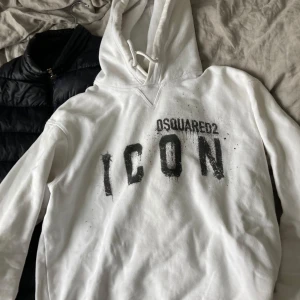 Vit hoodie från Dsquared2 med tryck - Vit hoodie från Dsquared2 med svart texttryck 'ICON' på bröstet. Klassisk huva med dragsko och ribbade muddar vid ärmslut och nederkant. Perfekt för en avslappnad och trendig stil.
