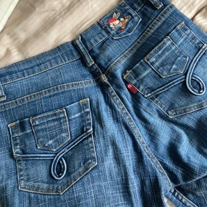 Blå bootcut jeans med broderad detalj - Säljer ett par låmidjade bootcut jeans med broderade detaljer på bakfickorna. Vintage stil och så sköna! Säljer pga att de inte längre är min stil☎️🩷Passar både s och m