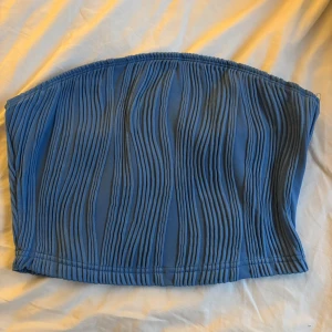 Blå tubtopp med struktur - Säljer en blå tubtopp med upphöjt strukturerat mönster. Toppen är ärmlös och har en tight passform som sitter snyggt på kroppen. Perfekt att styla till jeans eller kjol för en trendig look.