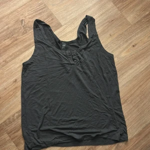 Svart linnetopp från H&M - Säljer en svart linnetopp från H&M med knappar framtill. Toppen har en enkel och avslappnad design med breda axelband och rundad halsringning. Perfekt för varma dagar eller som lager under en skjorta.