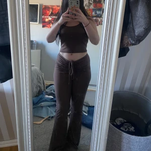 Brunt ribbat set med byxor och topp - Säljer ett brunt ribbat set med croppad linne-topp och matchande byxor. Byxorna har hög midja, dragsko och utsvängda ben. Perfekt för en avslappnad och trendig look.