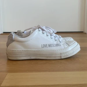 Vita sneakers från Love Moschino - Säljer ett par vita sneakers från Love Moschino med grå stickad hjärtdetalj på hälen. Perfekta nu inför sommaren!