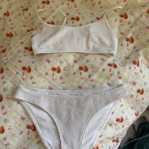 Vit bikini med struktur - Säljer en vit bikini med ribbad struktur och smala axelband. Både överdel och underdel har en enkel och stilren design. Perfekt för stranden eller poolen i sommar!