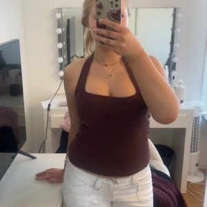 Mörkbrun halterneck topp - Säljer en mörkbrun halterneck topp med breda axelband och djup urringning. Toppen är figurnära och perfekt för varma dagar. Snygg att matcha med jeans eller kjol!