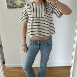 Randig blus från Tommy Hilfiger - Säljer en vit och marinblå randig blus från Tommy Hilfiger. Blusen har korta ärmar med volang och en lös passform.  Tröjan är i storlek 152 men sitter som en xs💗