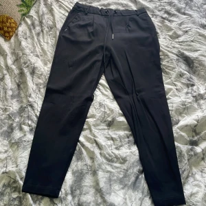 Svarta mjukisbyxor med snörning - Svarta mjukisbyxor med dragsko i midjan och raka ben. Byxorna har diskreta fickor på sidorna och är perfekta för en avslappnad stil. Materialet känns mjukt och bekvämt.