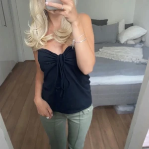 Svart tubtopp med knyt fram - Säljer en svart tubtopp med snygg knytdetalj framtill. Toppen är axelbandslös och har en åtsittande passform som framhäver figuren. Perfekt att matcha med jeans eller kjol för en trendig look.