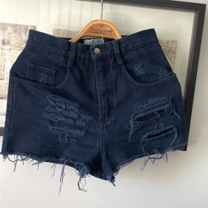 USAs favoriter;Jeansshorts från Carolina Colours modell Carolina blues strl 4 (36) - Ett par vintage jeansshorts i strl 4 (vilket är samma som 36) från det populära amerikanska märket Carolina Colours. Modellen heter Carolina Blues och är mörkblå men i vissa ljus ser de nästan svarta ut. De har ripped detaljer och lappen som sitter bak ska se ”sliten” ut så den ser ut som den ska, se foto. De är tvättade på ett sätt som gör att även om de inte innehåller något stretchmaterial är de mjukare än annat jeanstyg och känns supersköna att ha på sig. Knappt använda så nyskick 