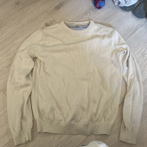 Vit  stickad tröja från Dressmann - Säljer en stilren beige stickad tröja från Dressmann i storlek XL. Tröjan har rund halsringning och ribbade muddar vid ärmslut och nederkant. Perfekt för lager-på-lager under kyligare dagar.