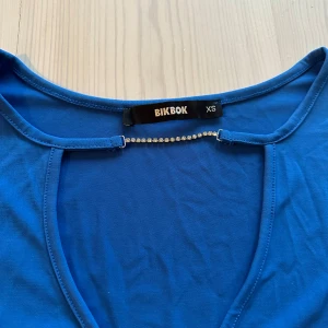 Blå långärmad topp med strassdetalj från Bik Bok - Snygg blå långärmad topp från Bik Bok med djup v-ringning och strasskedja framtill.
