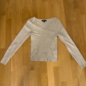 Beige ribbad långärmad topp från New Yorker - Säljer en beige långärmad topp från New Yorker med v-ringning och ribbad struktur. Perfekt basplagg som är enkel att matcha till olika outfits.