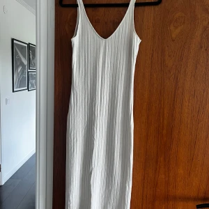 Beige ribbad klänning med v-ringning - Säljer en beige ribbad klänning  med v-ringning. Klänningen har en tight passform och en slits bak.  Strl S-M