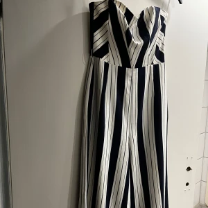 Randig onepisce från H&M - Säljer en snygg långklänning från H&M med breda svarta och vita ränder. Klänningen är axelbandslös och har en figurnära överdel med markerad midja. Perfekt för dig som gillar en stilren och modern look.