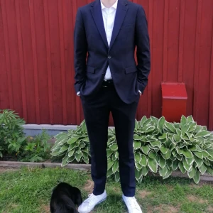 Mörkblå kostym med kavaj och byxor - Säljer en stilren mörkblå kostym med matchande kavaj och byxor. Kavajen har klassisk passform med två knappar och fickor framtill. Perfekt för formella tillfällen. Båda storlekarna är 50 byxa och kavaj. Finns ett litet hål inuti kavajen men osynligt och ej märkbart. Använd 1 gång