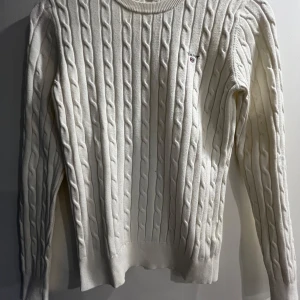 Vit kabelstickad tröja från GANT - Säljer en klassisk vit kabelstickad tröja från GANT i stretchig bomull. Tröjan har rund halsringning, långa ärmar och diskret GANT-logo broderad på bröstet. Perfekt för en stilren och tidlös look.