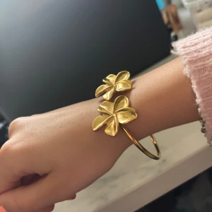 Guldfärgat armband med blommor från LYLA - Snyggt armband i guldfärg från LYLA med två stora blommor som dekoration. Perfekt accessoar för att lyfta din outfit. Säljer då den är lite stor för mig enligt mig. Köpt för 229kr säljer för 180kr, aldrig använd! Priset är diskuterbart!💘