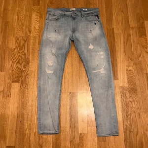 Ljusblå Replay jeansbyxor - Säljer ett par ljusblå Replay jeans med slitna detaljer och raka ben. Klassisk femficksmodell med knappgylf och Replay-logga på bakfickan. Perfekta för dig som gillar en avslappnad och trendig stil.