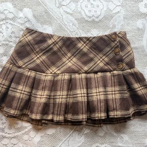 Minikjol med knappar - Supersöt brun rutig minikjol med knappar framtill. Kjolen har inbyggda shorts under!! Säljer för att den är för kort för mig, skulle rekommendera för xxs eller möjligen xs❤️köpt på vinted men den är helt ny! Varning, den är väldigt kort‼️