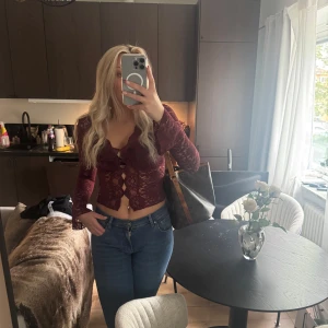 Vinröd spetsblus med volangdetaljer - Säljer en vinröd, transparent spetsblus med långa ärmar och volangdetaljer framtill. Blusen är slutsåld från ginatricot och har knappar framtill🥰