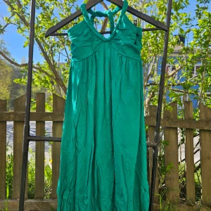 Grön långklänning med halterneck Y2K - Säljer en smaragdgrön långklänning med halterneck och djup v-ringning. Klänningen har en luftig passform och är perfekt för varma dagar. Materialet känns lätt och svalt mot huden. Perfekt för dig som vill sticka ut med färg! Y2K