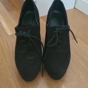 Svarta mocka klackskor med snörning - Säljer ett par svarta klackskor i mocka med snörning framtill. Skorna har spetsig tå och hög klack, vilket ger en elegant och stilren look. Perfekta för dig som vill ha något klassiskt men ändå trendigt.